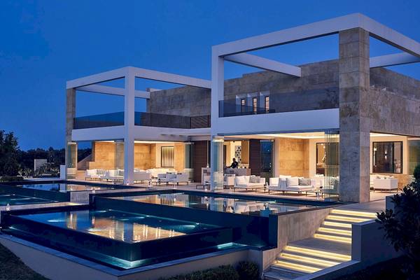 Außenansicht des Pelagos Suites Hotel & Spa bei Nacht mit beleuchteten Schwimmbädern und Couchlandschaft.
