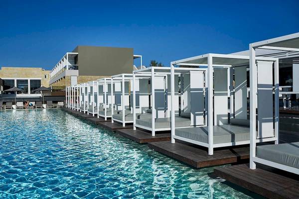 Pool-Lounge-Bereich im Pelagos Suites Hotel & Spa mit weißen Liegen und Sonnenschirmen.