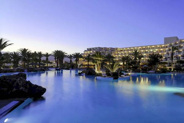 Außenpool des Melia Salinas Hotels bei Nacht mit beleuchteten Gebäuden und Palmen im Hintergrund.