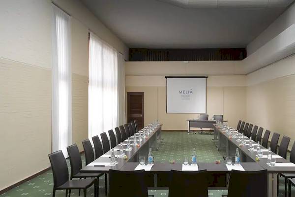 Konferenzraum im Melia Salinas Hotel mit langen Tischen und Stühlen, Projektionsleinwand und Möbeln.