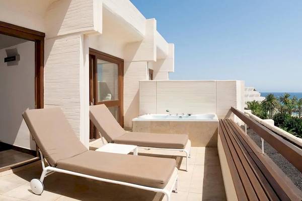 Balkon des Melia Salinas Hotels mit Jacuzzi und Meerblick, zwei Liegen und Blick auf das Schwimmbad.