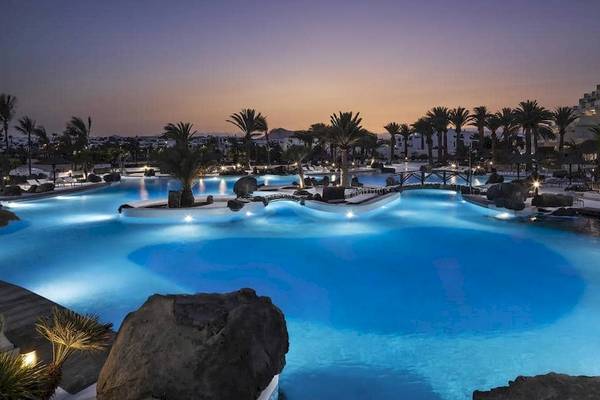 Nachtansicht des beleuchteten Außenpools des Melia Salinas Hotels mit Palmen und Felsen