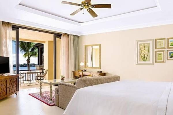 Suite-Schlafzimmer im Westin Turtle Bay Resort & Spa, Mauritius mit Blick auf den Ozean, einem großen Bett, einer Couch, einem Fernseher und einem Schreibtisch.