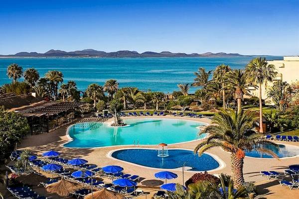 Ein Resort mit großem Schwimmbad und Meerblick, umgeben von Palmen und Liegestühlen.