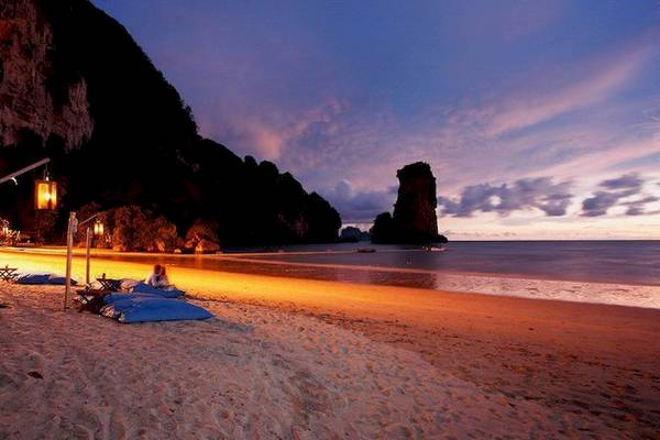 Abendstimmung am Strand des Centara Grand Beach Resort & Villas Krabi mit einer Person, die auf Kissen sitzt, umgeben von Laternen.