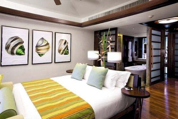 Schlafzimmer im Centara Grand Beach Resort & Villas Krabi mit großen Bett, Kissen, Lampen und Gemälden.