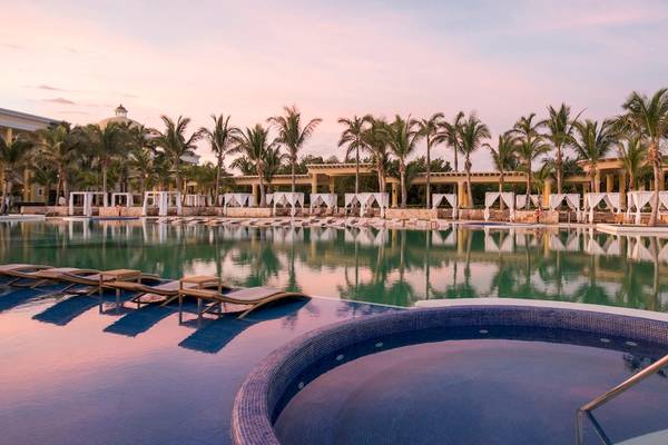 Der Poolbereich des Iberostar Grand Paraiso Hotels am Abend mit Loungeliegen und Palmen