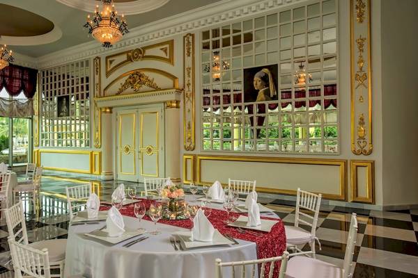 Speisesaal im Iberostar Grand Paraiso mit runden Tischen, eleganten Stühlen und Goldverzierungen.