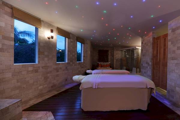 Massageraum im Iberostar Grand Paraiso Hotel mit zwei Massageliegen, farbigen Lichtern und Fenstern.