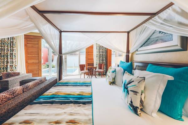 Suite im Iberostar Grand Paraiso mit einem Himmelbett und Baldachin, umgeben von Möbeln und einem Pool.