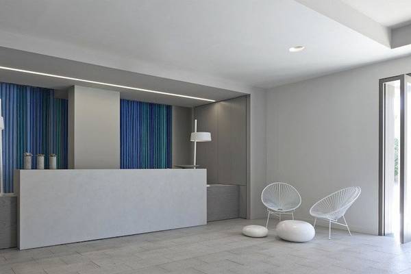 Empfangsbereich des Bay Hotel & Suites mit modernem Design, weißen Möbeln und blauen Vorhängen.