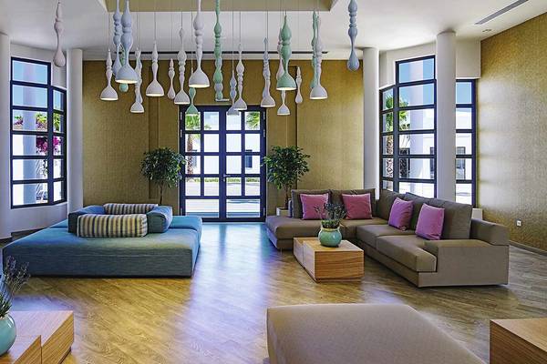 Lobby des Club Plimmiri Hotels mit modernen Möbeln, Holzboden und großen Fenstern.