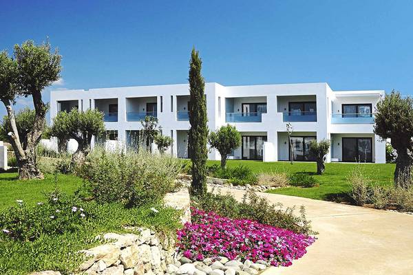 Außenansicht des weißen Club Plimmiri Hotels mit gepflegtem Rasen und Bäumen davor.