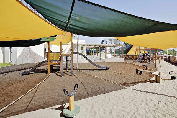 Kinderspielplatz im Club Plimmiri Hotel mit Sand, Rutschen und Schaukeln unter einem Sonnensegel.