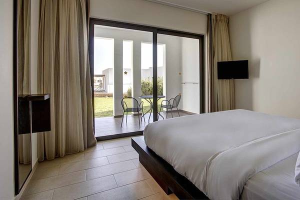 Ein Zimmer im Club Plimmiri Hotel mit einer Terrasse, auf der zwei Stühle und ein Tisch stehen, und einem großen Bett.