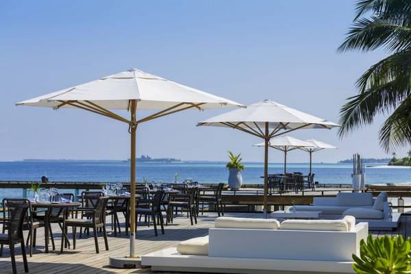 Terrasse des Outrigger Maldives Maafushivaru Resorts mit Blick auf das Meer und weißen Möbeln.