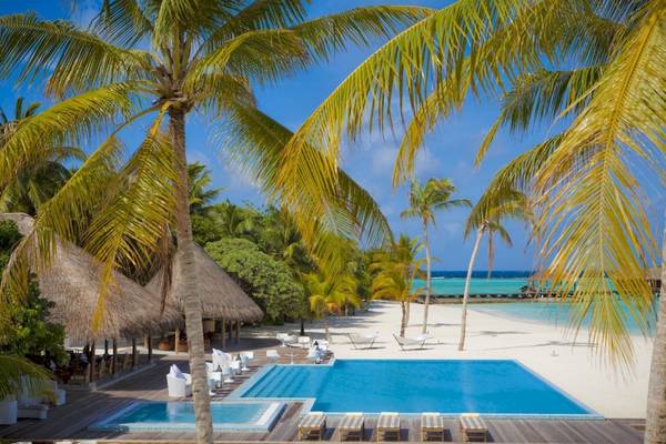 Außenpool und Liegestühle am Strand des Outrigger Maldives Maafushivaru Resorts