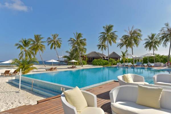 Außenpool des Outrigger Maldives Maafushivaru Resorts mit weißen Sonnenliegen und Sonnenschirmen.