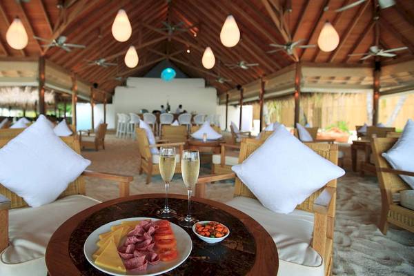 Restaurant im Outrigger Maldives Maafushivaru Resort mit weißen Kissen, Tischen und Stühlen.