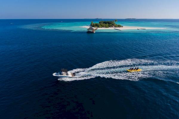 Aussicht von oben auf das Outrigger Maldives Maafushivaru Resort mit Booten im Wasser.