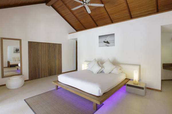 Schlafzimmer im Outrigger Maldives Maafushivaru Resort mit weißem Bett, Kissen und Decken.