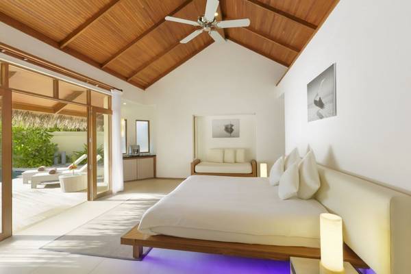 Schlafzimmer im Outrigger Maldives Maafushivaru Resort mit Doppelbett, Sofa, Deckenventilator und Fenstern
