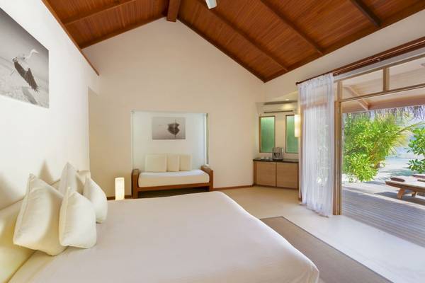 Innenansicht eines Schlafzimmers im Outrigger Maldives Maafushivaru Resort mit offenem Fenster und Blick auf den Garten.