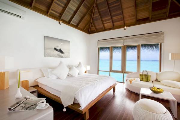 Schlafzimmer mit Meerblick im Outrigger Maldives Maafushivaru Resort mit großem Bett, weißen Möbeln und Fenstern zum Ozean.