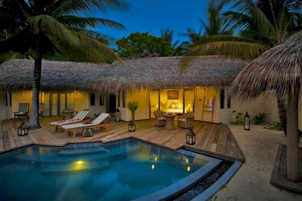 Nachtansicht des Outrigger Maldives Maafushivaru Resorts mit Pool und Loungebereich.