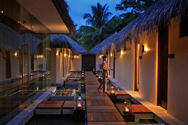 Nachtansicht des Kurumba Maldives Hotels mit Gehweg und brennenden Laternen.