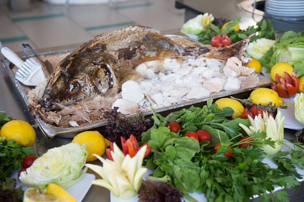 Ein Tisch mit Salaten, Tomaten, Zitronen und einem ganzen gegrillten Fisch.