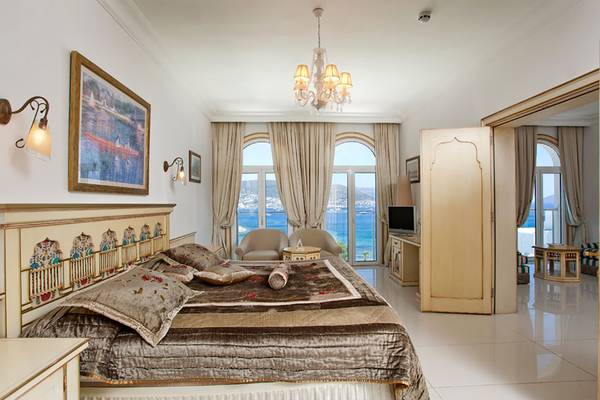 Schlafzimmer im Salmakis Resort & Spa mit Meerblick, großem Bett, zwei Sesseln und Fernseher.