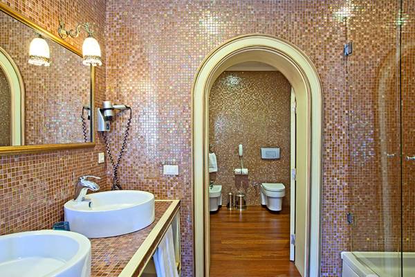 Ein Badezimmer mit mosaikverkleideten Wänden, zwei Waschbecken, einem Spiegel und einer Dusche.