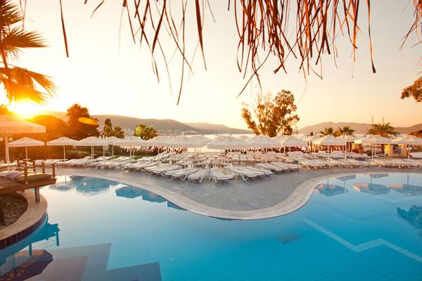 Sonnenuntergang am Pool des Salmakis Resort & Spa mit vielen Sonnenliegen und weißen Schirmen.