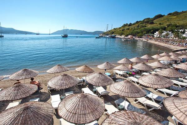Strand des Salmakis Resort & Spa mit vielen Sonnenschirmen und Liegen, Blick auf das Meer und Berge