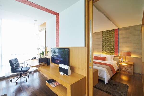 Innenansicht eines Zimmers im Pathumwan Princess Hotel mit Schreibtisch, Stuhl, Fernseher und Bett.