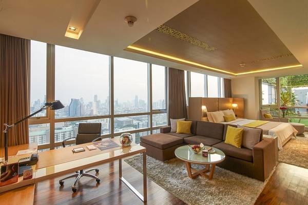 Hotelzimmer der Pathumwan Princess mit Blick auf die Stadt, inklusive Schreibtisch, Bett und Wohnzimmerbereich.