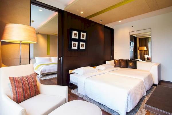 Schlafzimmer im Pathumwan Princess Hotel mit zwei Betten, weißem Sofa und Nachttisch.