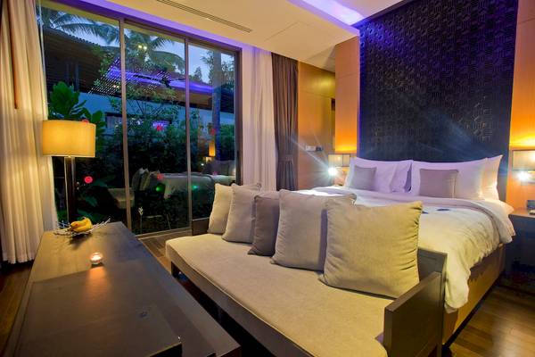 Schlafzimmer im Ramada Resort by Wyndham Khao Lak mit einem großen Bett, Sofabett, Tisch und Glaswand