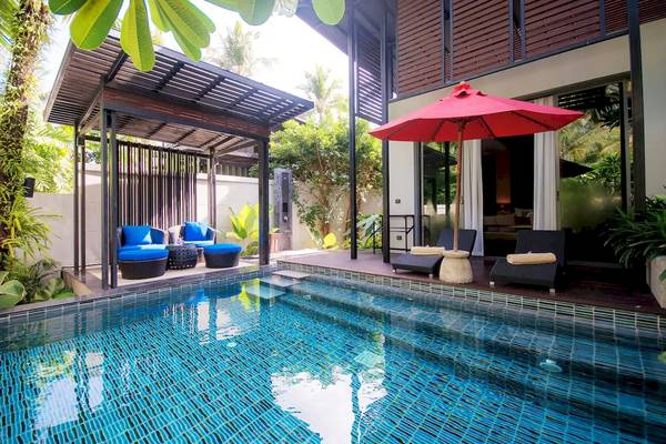 Pool-Terrasse im Ramada Resort Khao Lak mit Lounge-Stühlen und einem roten Sonnenschirm.