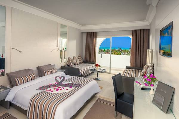 Hotelzimmer im Djerba Plaza Thalasso & Spa mit einem Bett, zwei Sofas, einem Schreibtisch und einem Ausblick auf das Meer.