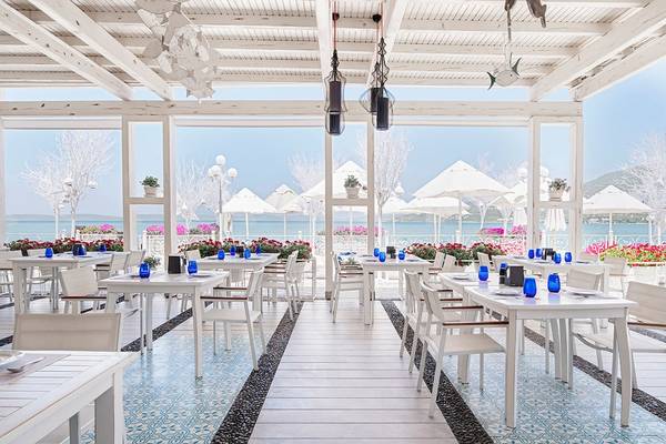 Außenterrasse des Voyage Torba Hotels mit weißen Tischen und Stühlen und Blick auf das Meer.