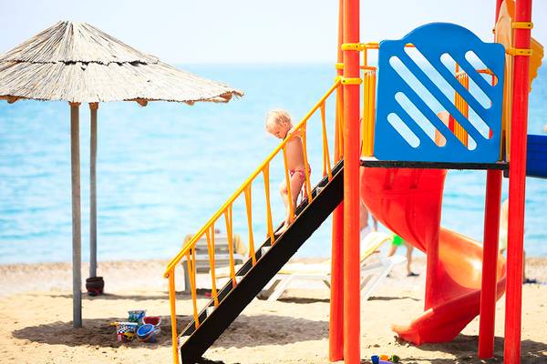 Ein kleines Kind klettert auf einer Treppe auf einem Spielplatz am Strand.