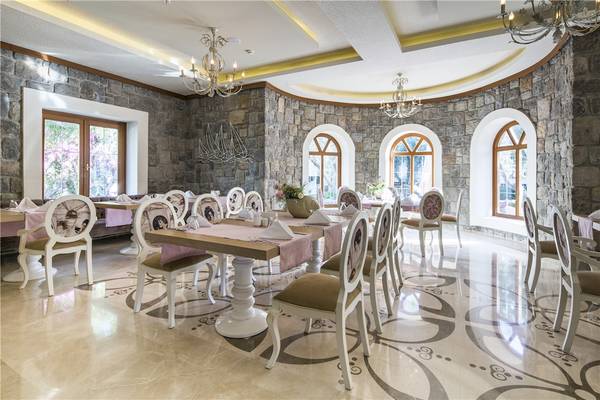 Innenraum des Voyage Torba Hotels mit steinernen Wänden, Bogenfenstern und elegant eingerichteten Tischen und Stühlen.