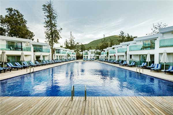 Pool- und Loungebereich des Voyage Torba Hotels mit weißen Gebäuden und blauen Sonnenliegen.