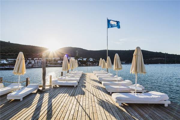Terrasse des Voyage Torba Hotels mit weißen Liegen und Sonnenschirmen am Meer