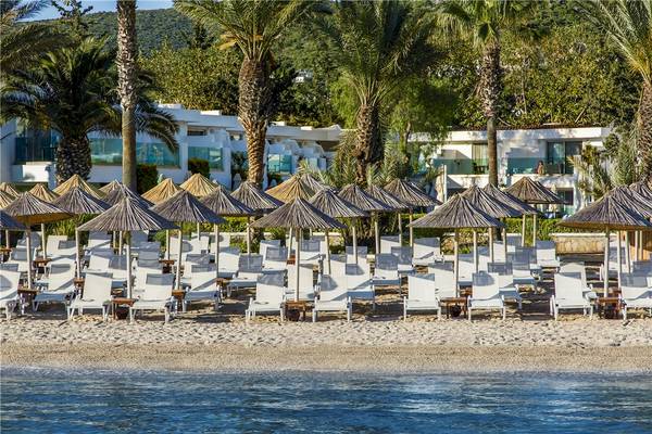 Strand mit vielen weißen Liegestühlen und Sonnenschirmen vor dem Voyage Torba Hotel