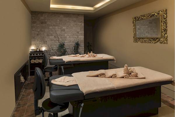 Massageraum im Voyage Torba Hotel mit zwei Massagetischen, einer Steinwand und einem goldenen Spiegel.