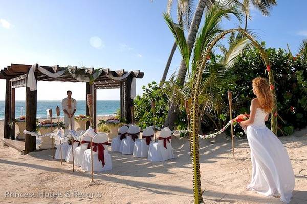 Eine Braut in einem weißen Kleid geht durch eine Hochzeitszeremonie auf dem Strand von Punta Cana Princess.