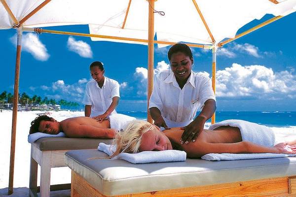 Zwei Personen erhalten eine Massage am Strand unter einem Sonnenschirm im Hotel Punta Cana Princess.